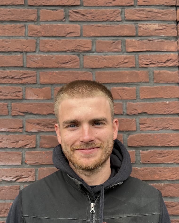 Bas lacht in zijn werkjas voor een bakstenen muur